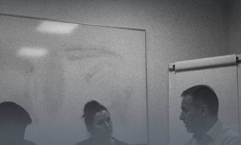 A woman looking up while a man behind her takes a phone call