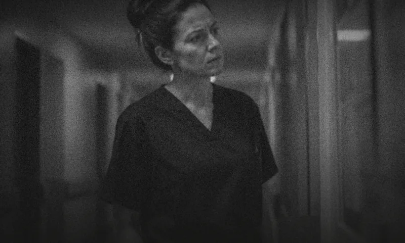 A nurse in scrubs standing alone in a corridor