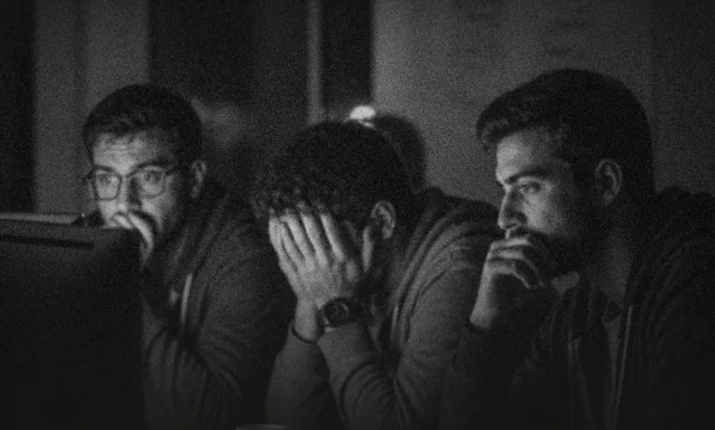 Three men looking worried at a laptop late at night